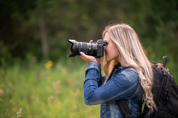 A woman using a camera equipped with the Nikon Z 24-120mm f4 S lens stands in the clearing of a forest.