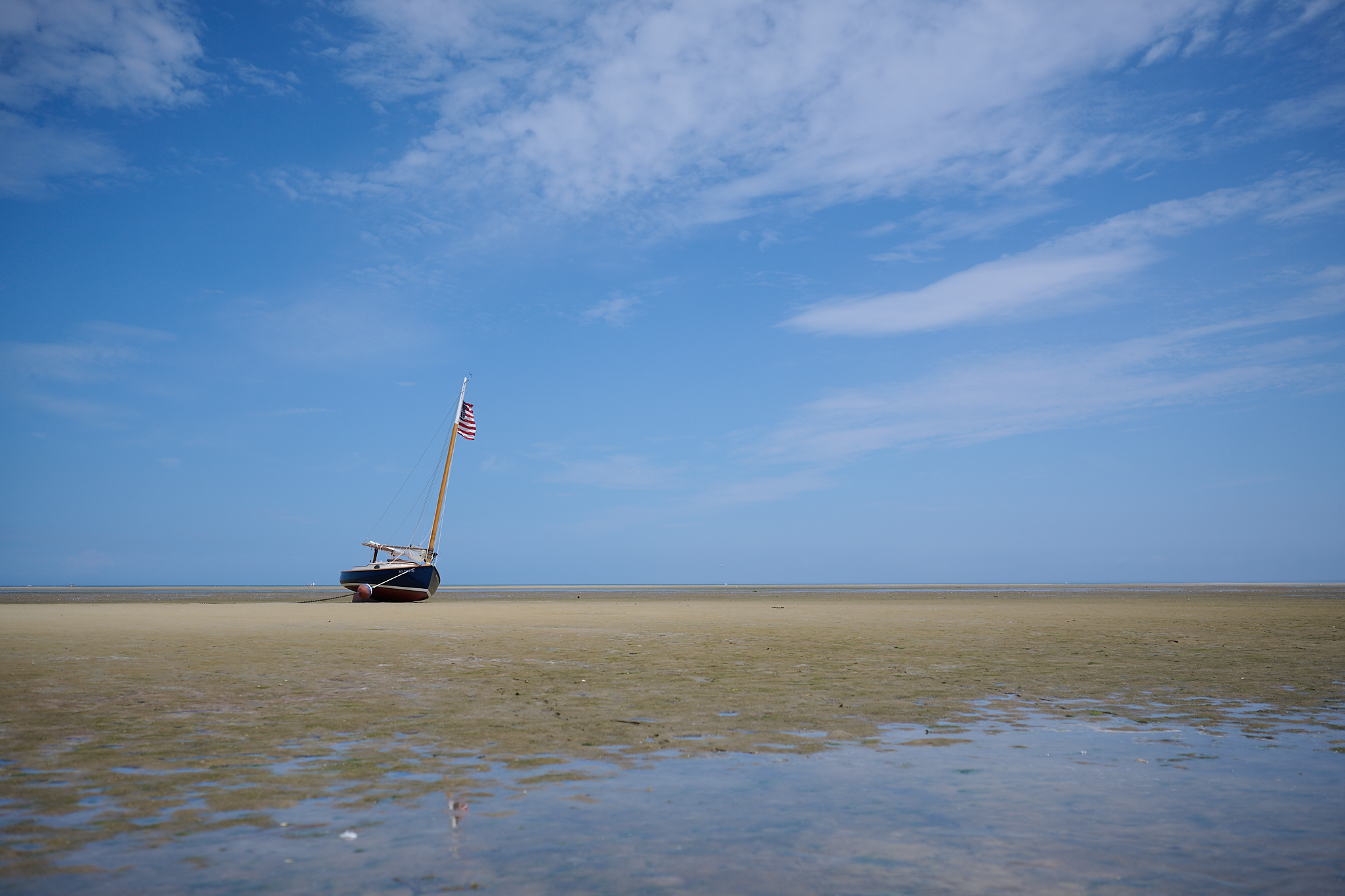 A ship moored to the beach with blue skies above and a reflection in a puddle.
