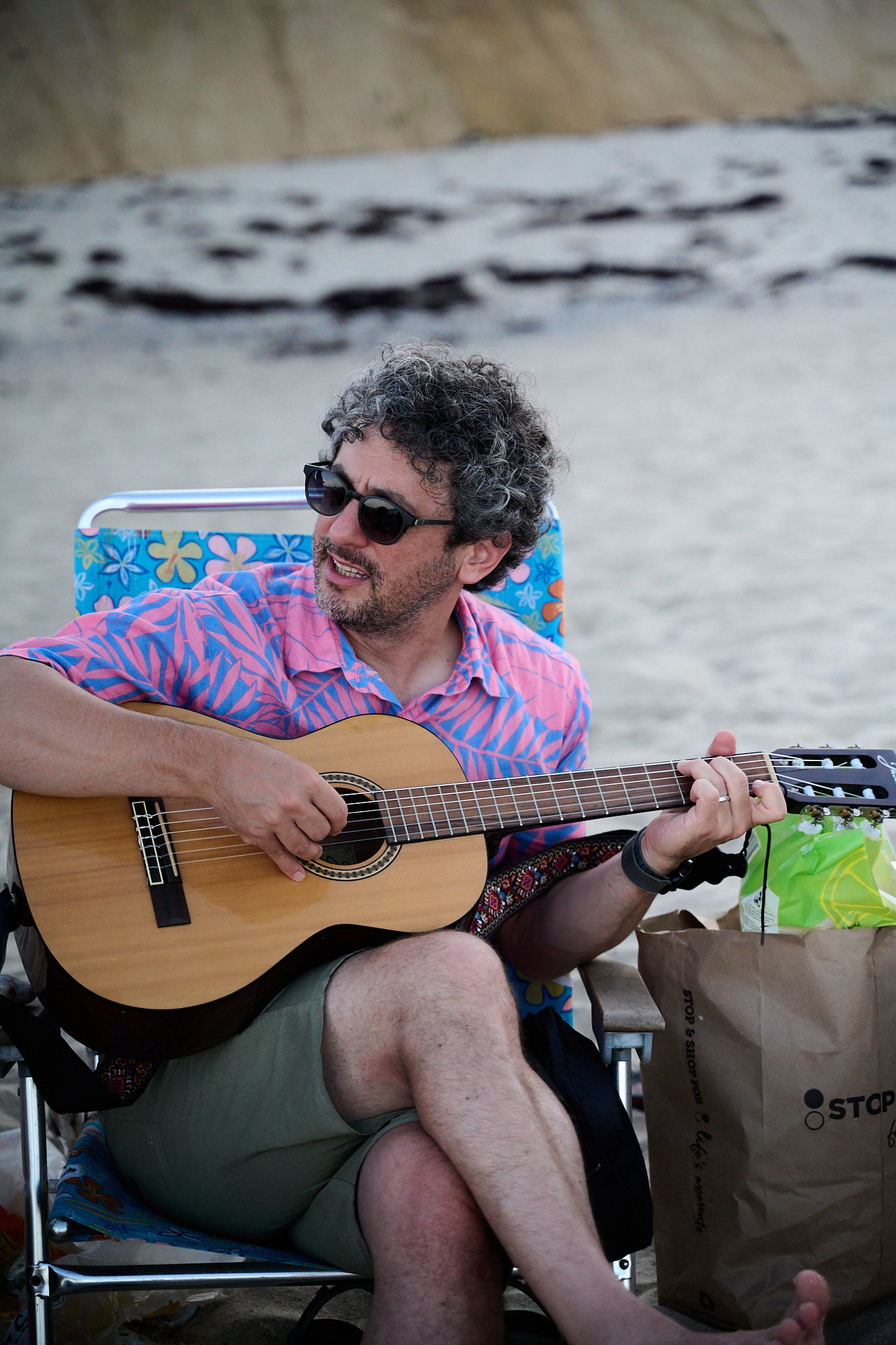 A man in a brightly colored shirt plays the guitar at a beach.